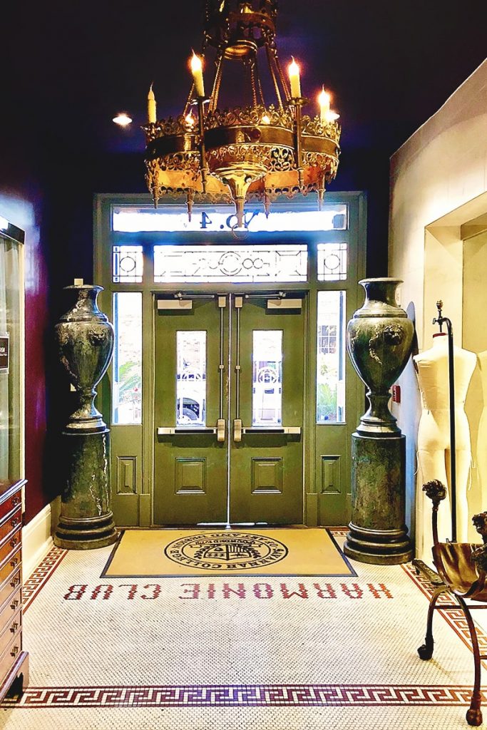 Elaborate entryway painted deep purple with green doors, with floor tiles reading "Harmonie Club"