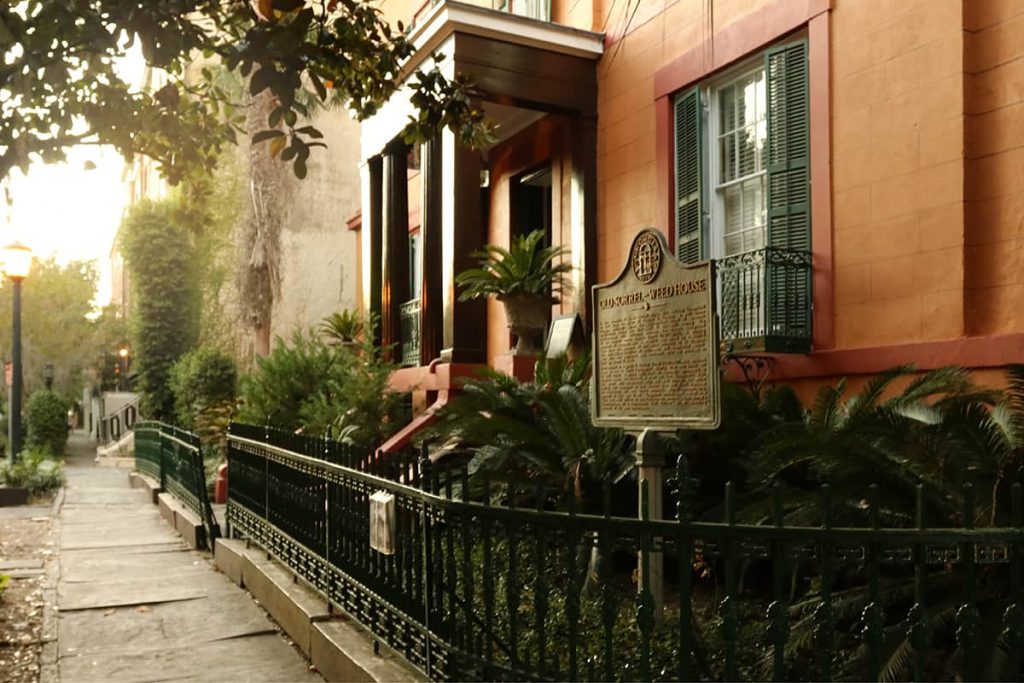 The entrance to the Sorrel-Weed House shows a rust-colored stucco home with cast iron gates and a historic marker by the front door. It's considered one of the most haunted places in Savannah Georgia