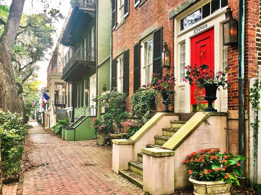 A stately brick home with pretty landscaping, black shutters, a bright red door, and the number eleven above the doorway