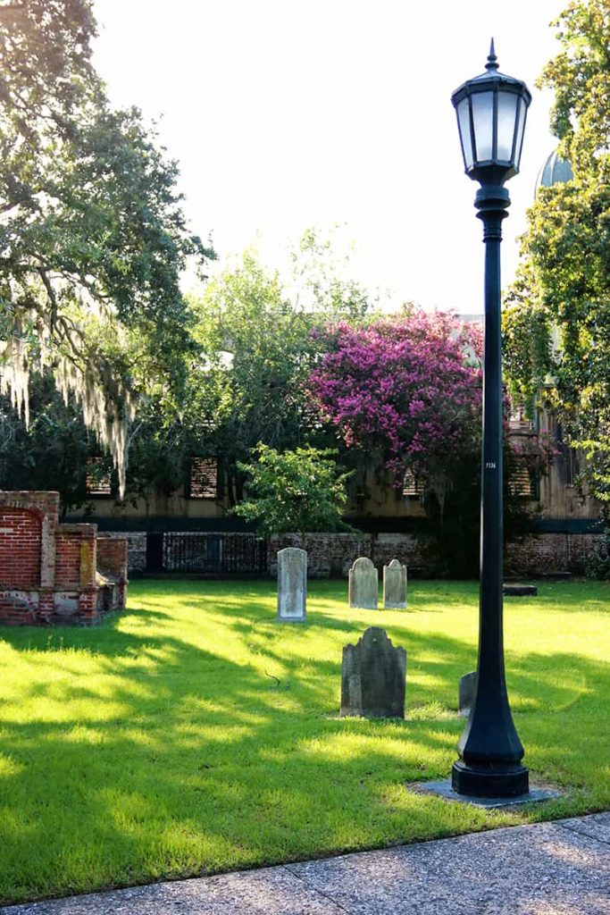 Cemetery scene with old headstones, a lamppost, and Spanish moss dangling from the trees.