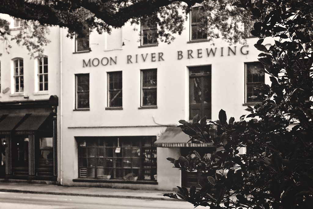 Peeking through the trees at a four-story building labeled Moon River Brewing