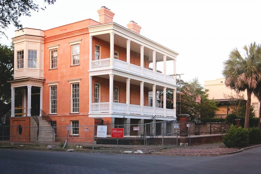 Three-story house undergoing renovation with peach colored stucco and a white porch extending the entire length of the side of the house