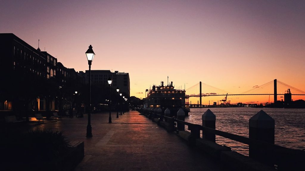 Riverfront plaza along River Street at dusk with the Savannah River and Talmadge bridge in the distance