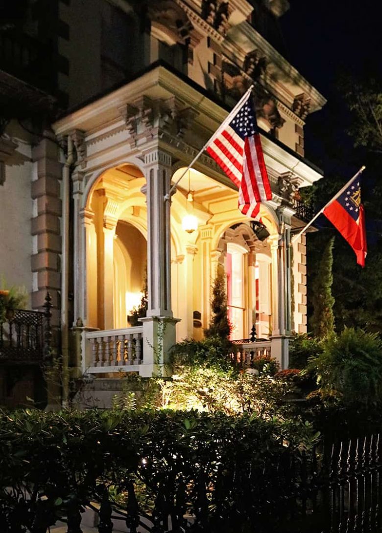 Front entrance to the Hamilton-Turner Inn lit up at night with two flags on display over the porch