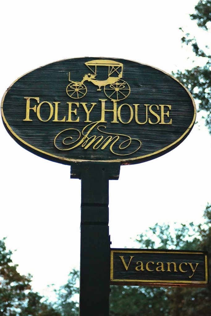 Oval-shaped wooden sign with gold text reading Foley House Inn and an image of a horse-drawn carriage