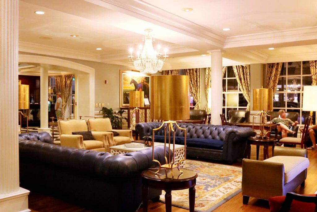 The warmly lit lobby of The Marshall House in Savannah with two navy blue leather couches, gold upholstered chairs, a beautiful chandelier, and nice artwork on the walls