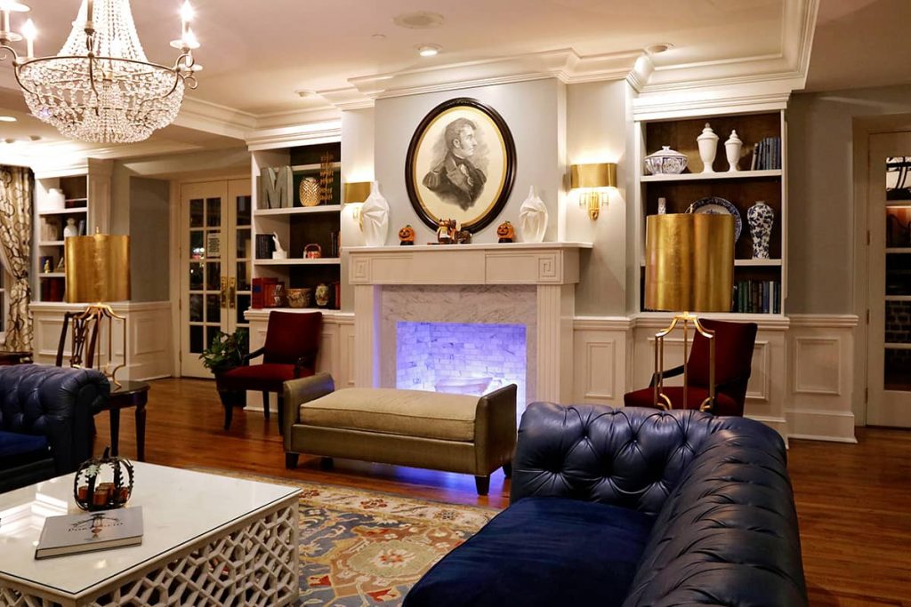 Warm and welcoming lobby of The Marshall House in Savannah GA with a fireplace surrounded by bookshelves and two blue leather couches nearby