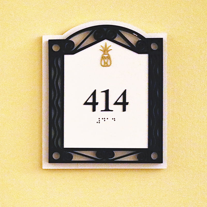 White sign with black frame and a gold pineapple above the room number 414