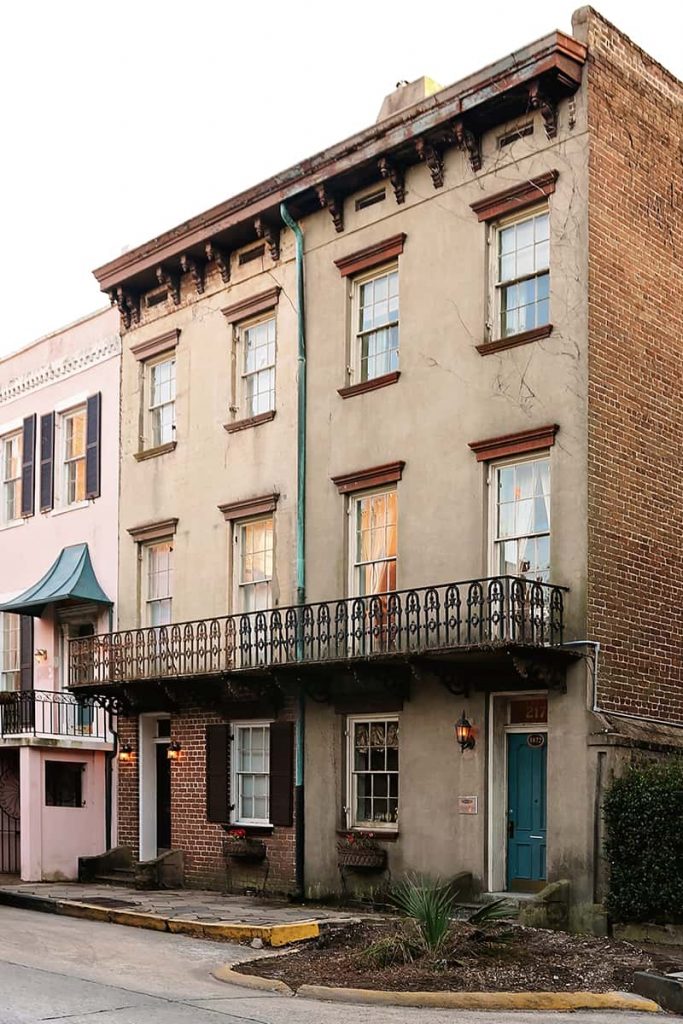 Three-story brown stucco and brick home with a blue door and an iron balcony on the second floor