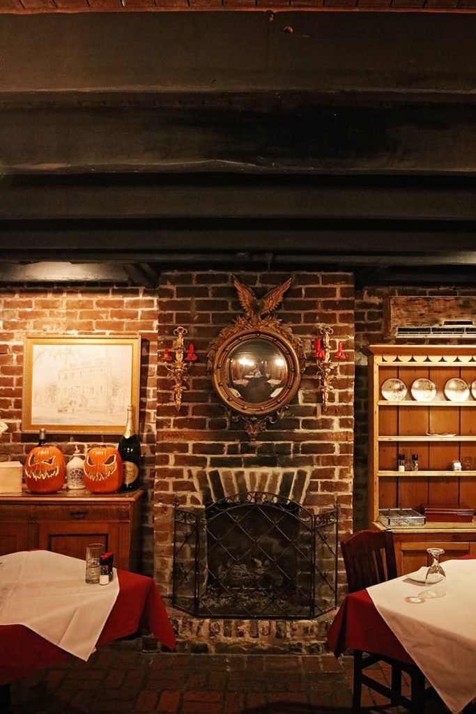 Low wood-beam ceilings above a fireplace with gold-framed mirror at the haunted 17Hundred90 Inn and Restaurant.