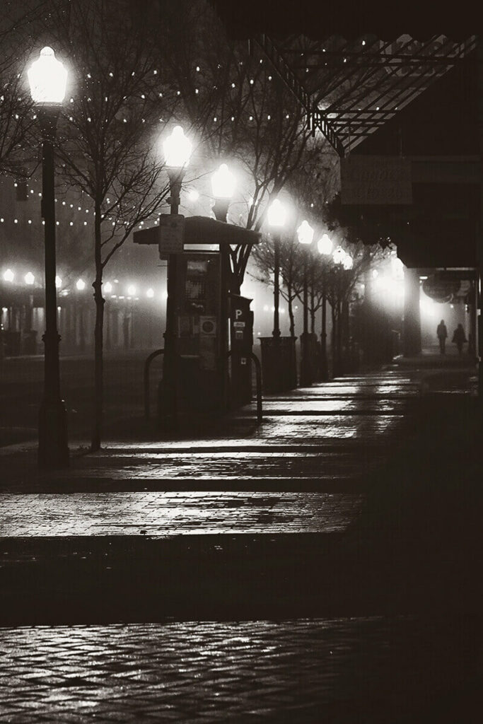 Nighttime scene along Broughton Street with street lamps glowing in the mist and a silhouette of two people in the distance