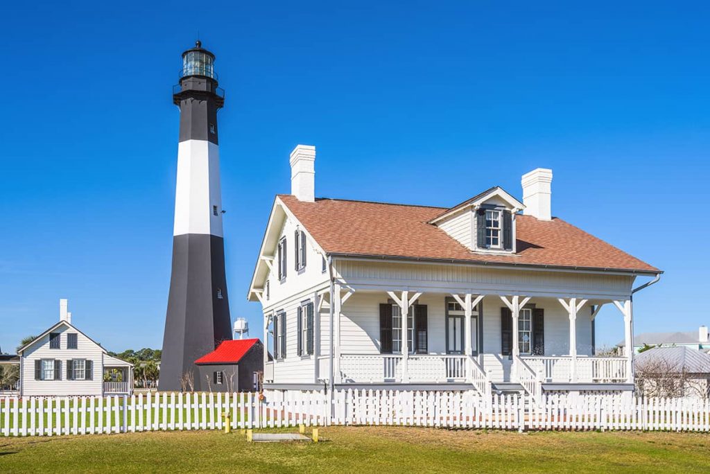 White cottage with a black and white lighthouse behind it and deep blue skies in the background