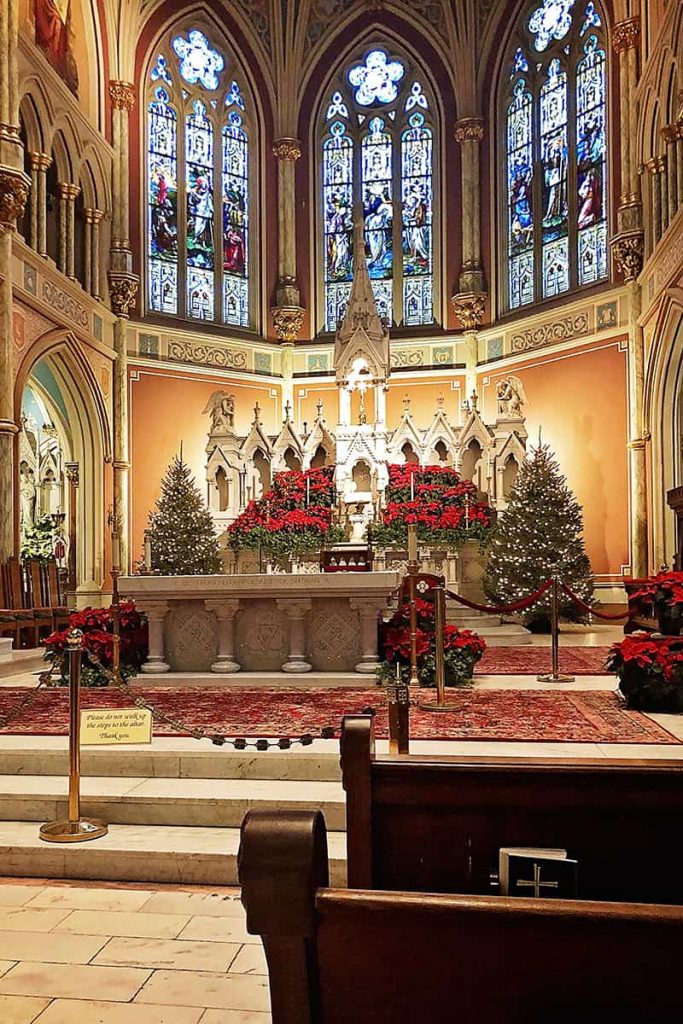 Interior of the Cathedral Basilica of St. John the Baptist with large stained glass windows, Christmas trees, and poinsettias