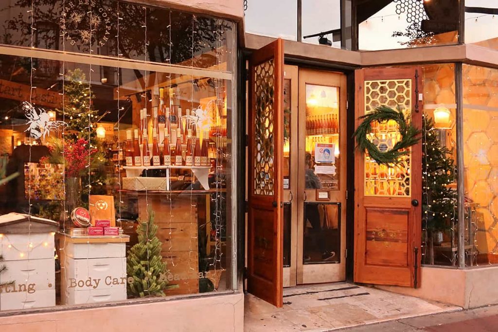 The Savannah Bee Company storefront with a Christmas wreath on the front door and Christmas trees in the window