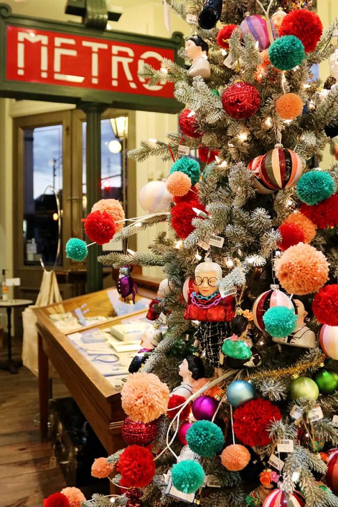 Christmas tree inside The Paris Market in Savannah with colorful red, peach, and teal fluff ball decor and a Paris Metro sign in the background