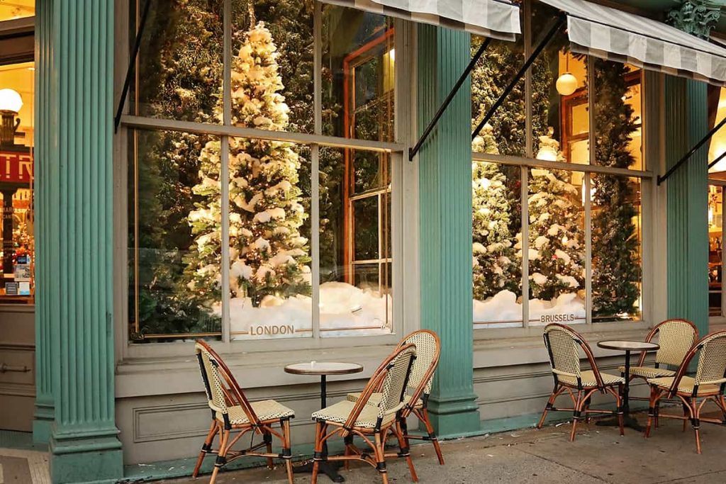 Elaborate holiday window displays of flocked Christmas trees at The Paris Market with cafe seating under a striped awning