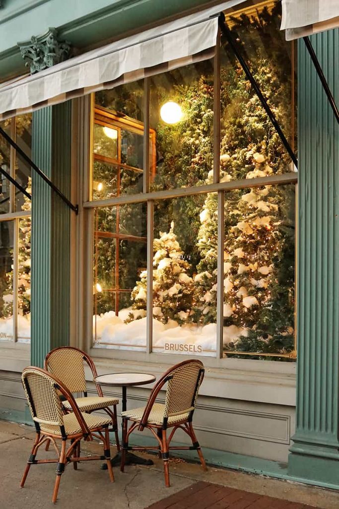 Elaborate holiday window display of Christmas trees at The Paris Market with cafe seating under a striped awning