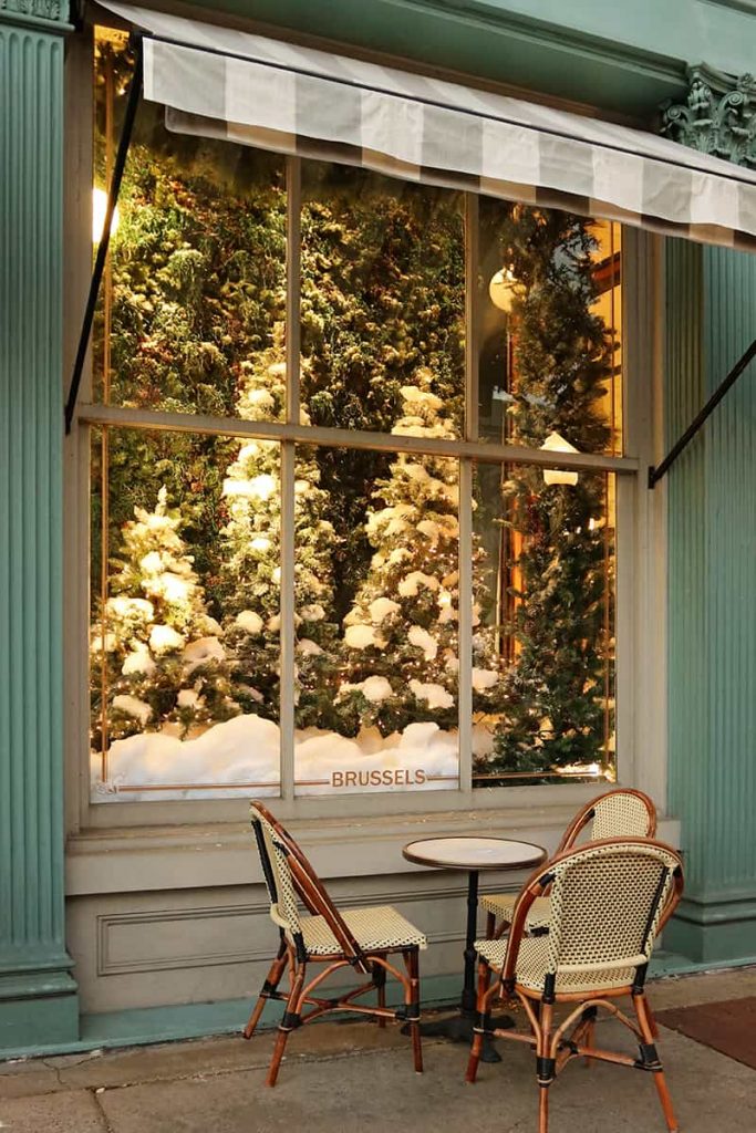 Elaborate holiday window display of Christmas trees at The Paris Market with cafe seating under a striped awning