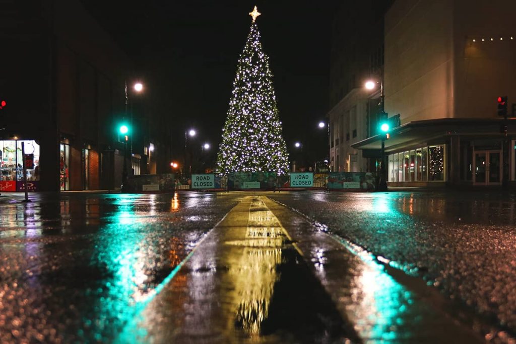A lit Christmas tree at night reflected in a wet paved city street