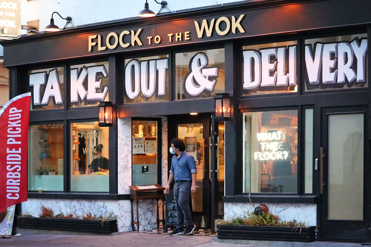 Flock to the Wok storefront in Savannah GA with a man standing in the entryway wearing a mask for Covid health reasons.