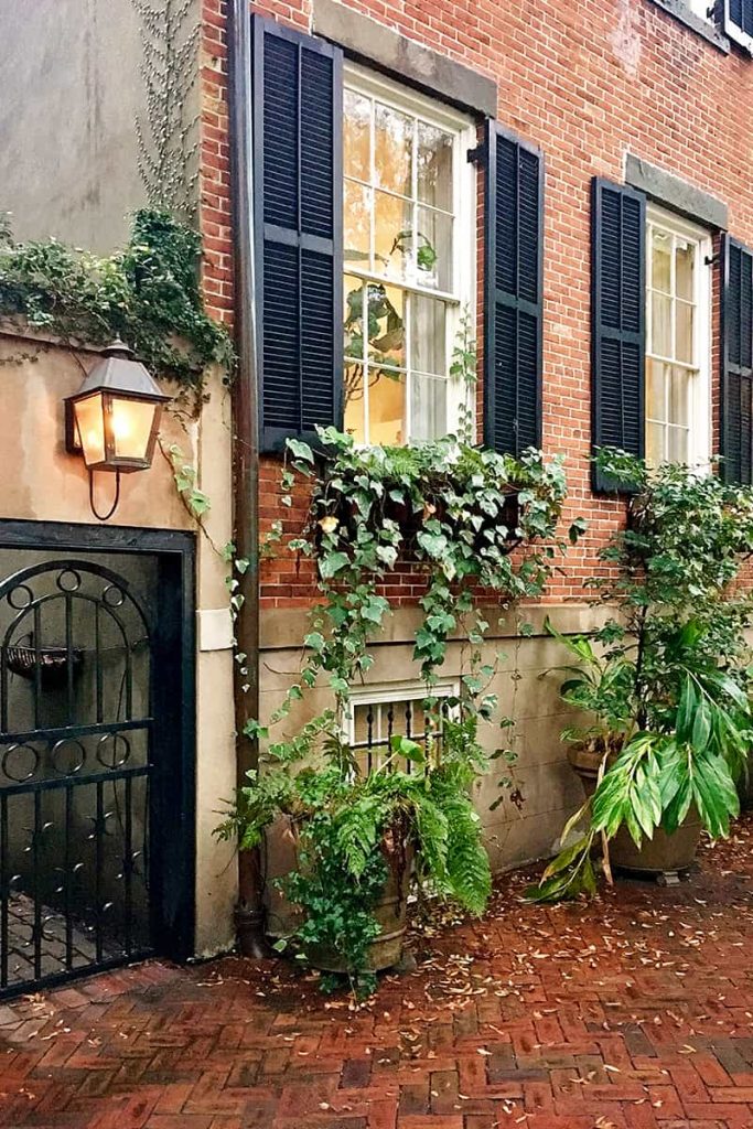 Rainy day scene of a historic brick home on Jones Street with black shutters and greenery hanging from the window boxes