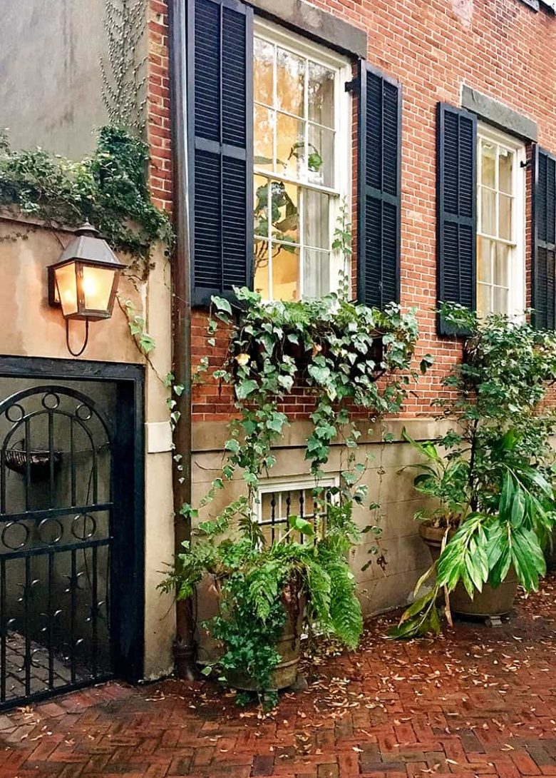 Rainy day scene of a historic brick home on Jones Street with black shutters and greenery hanging from the window boxes