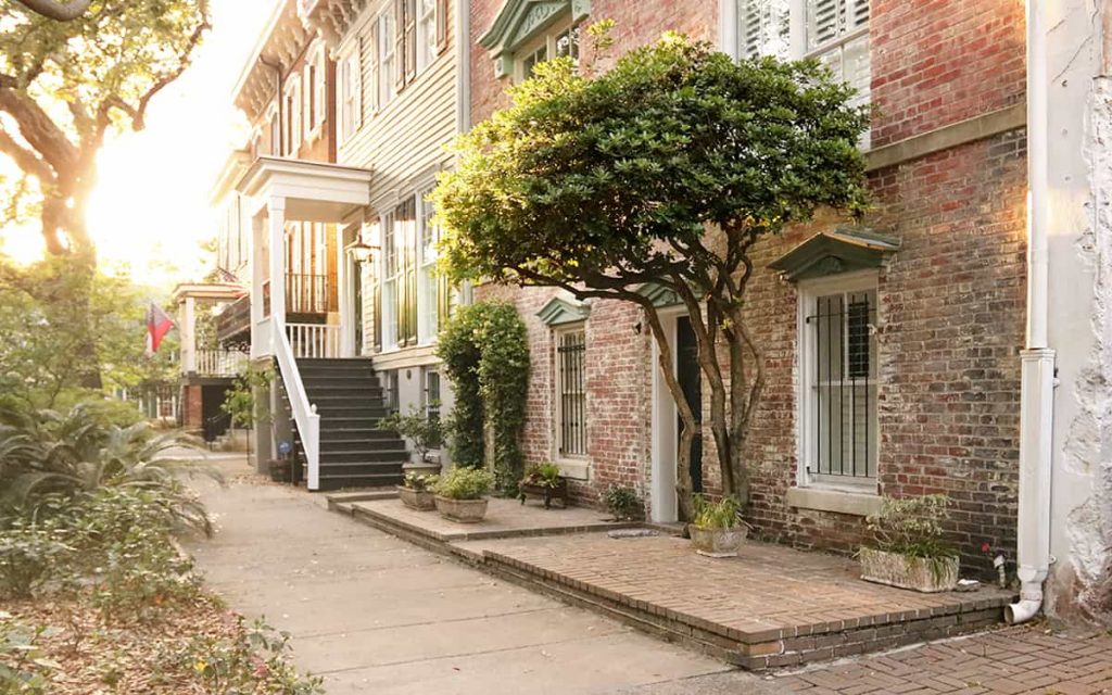 View down the sidewalk of Jones Street with a warm sunset glowing through the trees and illuminating a historic home