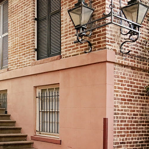 Metal street sign with gas lamplights attached to the corner of a home