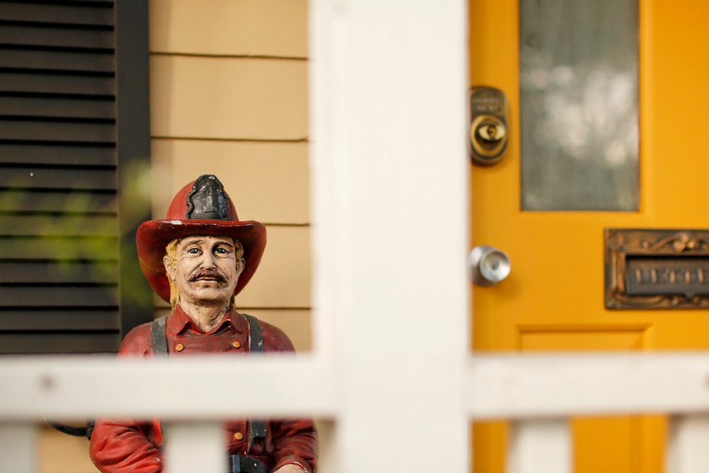 A colorful old statue of a firefighter peers over the front porch railing of a house on Jones Street, standing guard next to a cheery yellow door
