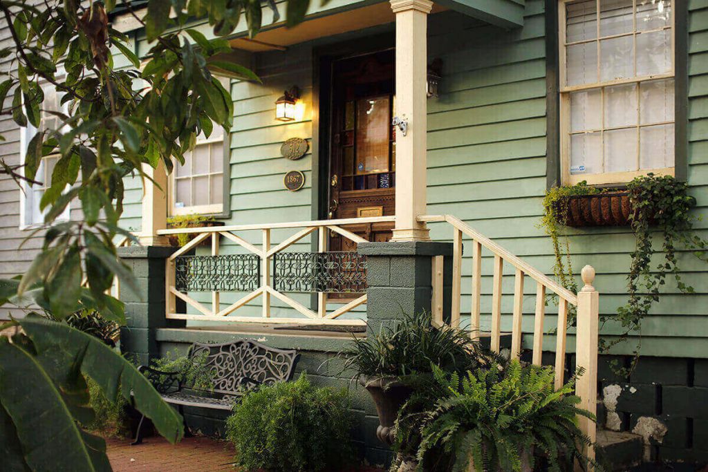 Front porch view of a modest pale green home on Jones Street surrounded by lush greenery