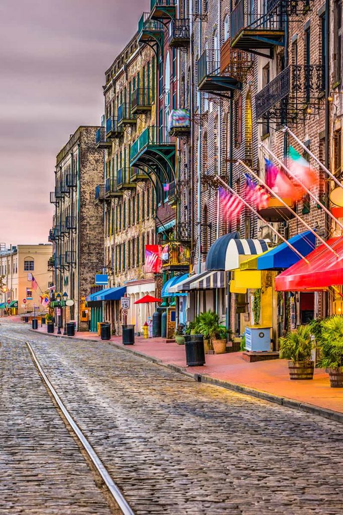 Cobblestone street with warehouse buildings and colorful flags above storefronts