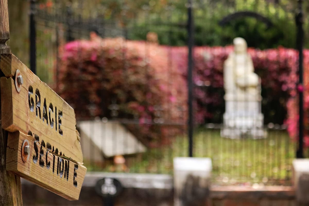 Wooden sign with "Gracie Section E" etched into it in the foreground and the grave of Little Gracie Watson in the background