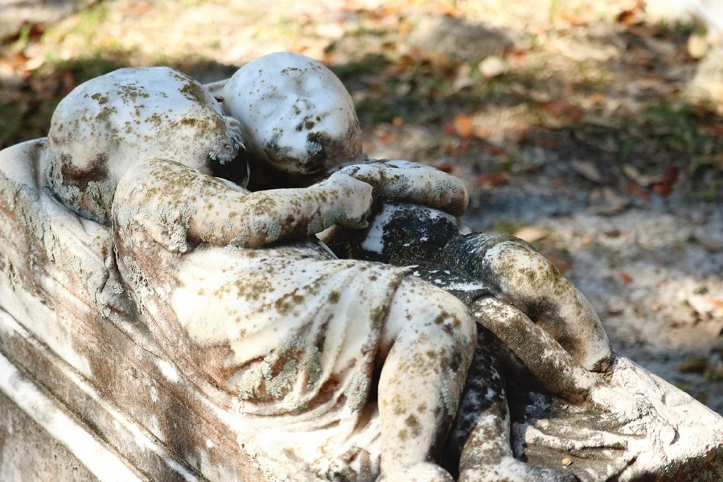 Headstone of two babies lying side by side, facing one another and holding hands