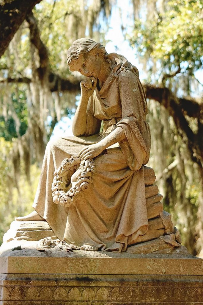 Statue of a woman sitting and thinking with her head resting on her right hand and a wreath in her left hand