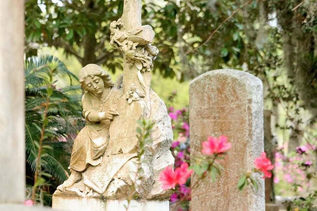 Statue of a young girl sitting next to a cross who appears to be writing on the stone marker