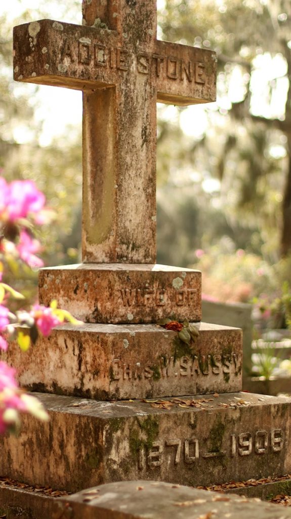 An old weathered stone cross with lichens growing on it at Bonaventure Cemetery