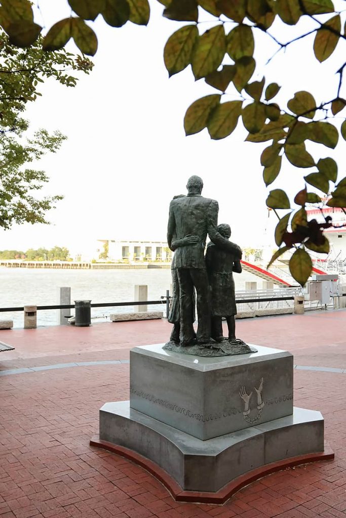Back view of the African American Monument with a father's arms wrapped around his family as they look out towards the Savannah River