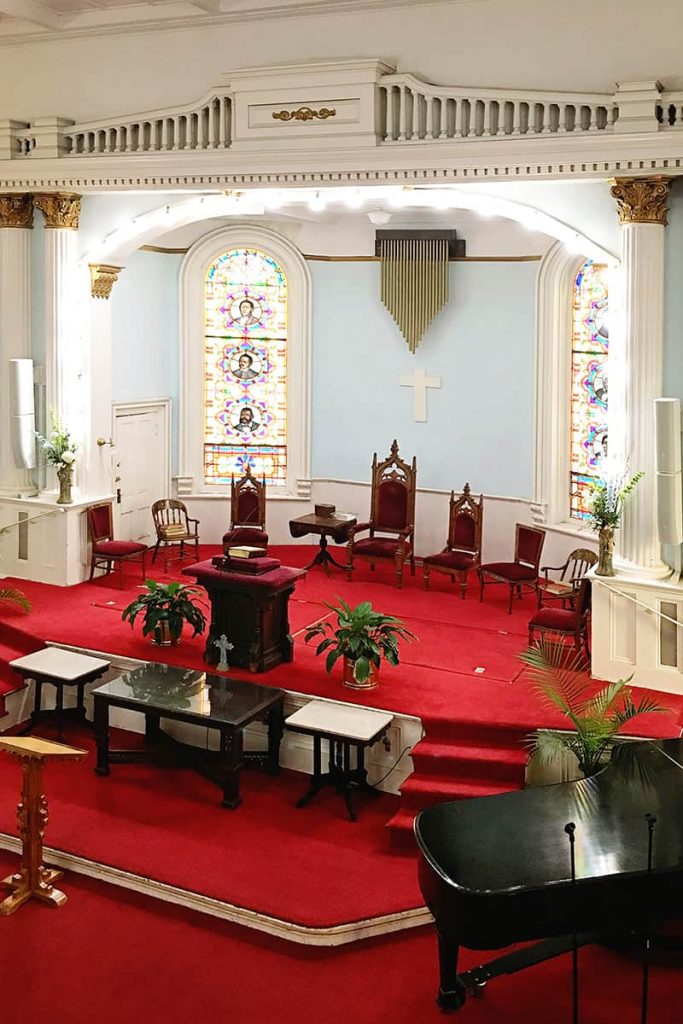 Sanctuary of First African Baptist Church with bright red carpet, pale blue walls, and a pulpit surrounded by stained glass