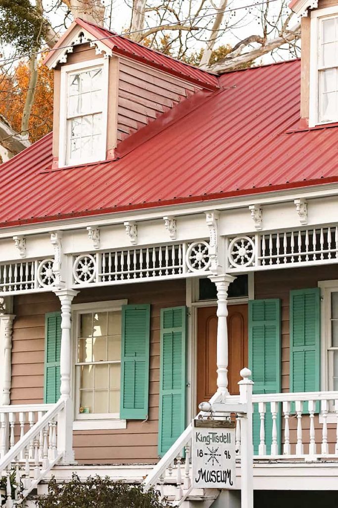 Victorian-style front porch of the King-Tisdell Cottage with a cheery red metal roof and green shutters surrounding the doors and windows