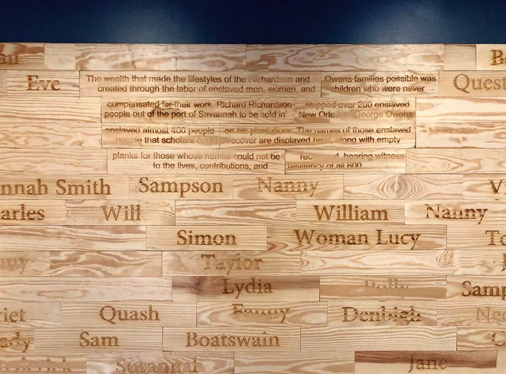 Wall made from wooden planks, some with names burned into them and some blank. Each plank honors an enslaved person who worked for the Owens family