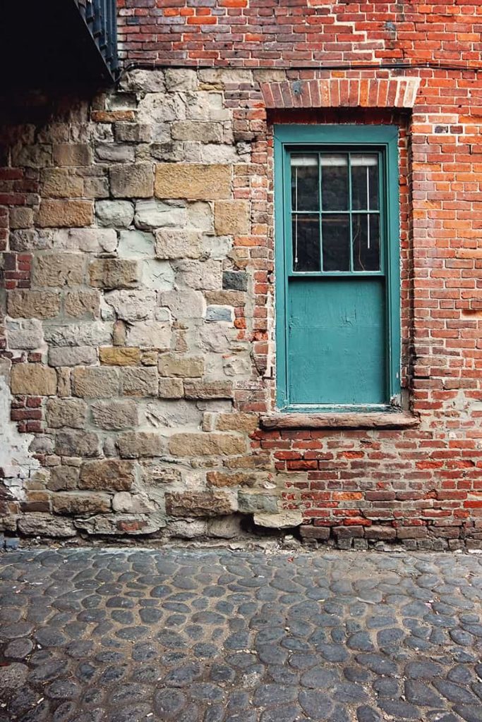 A green-framed window surrounded by a mixture of old bricks and stones along historic Factors Walk
