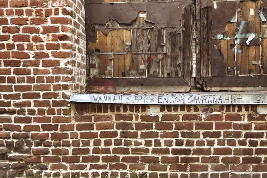 Graffiti painted beneath a boarded window on Factors Walk that says Vannah Say, Enjoy Savannah!