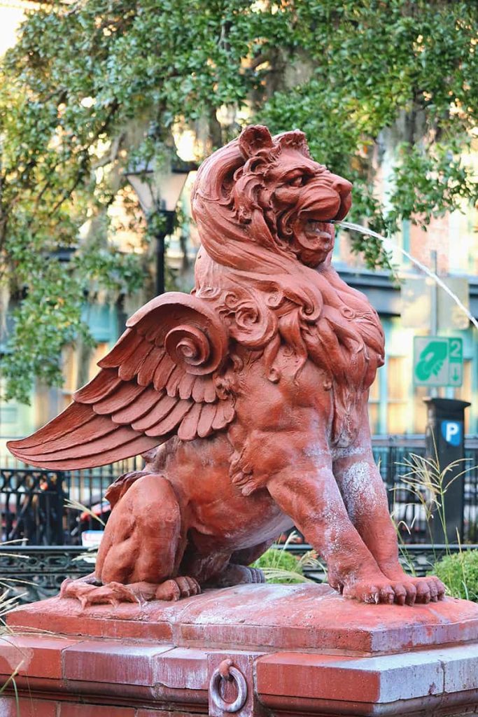 Side view of a terra cotta winged lion statue with a stream of water spraying from its mouth