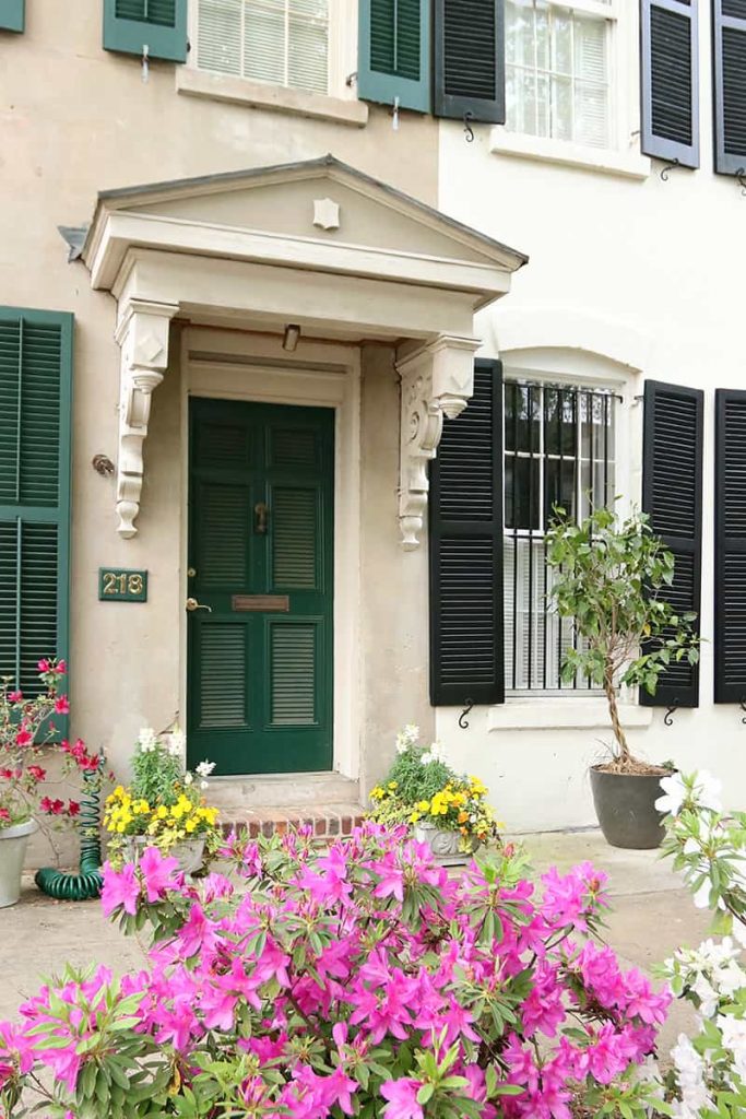Green door to a row home with Victorian trim and yellow and pink flowers around the entrance