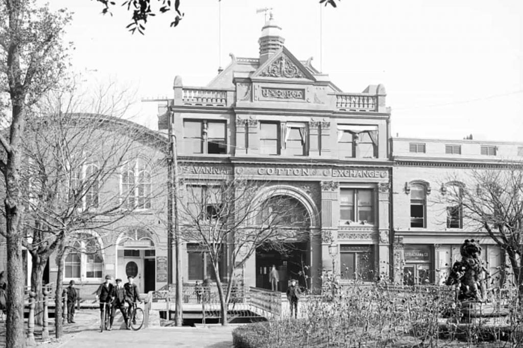 Historic B&W photo of the exterior of the Old Savannah Cotton Exchange building circa 1904 with men in suits and hats standing out front on Factors Walk