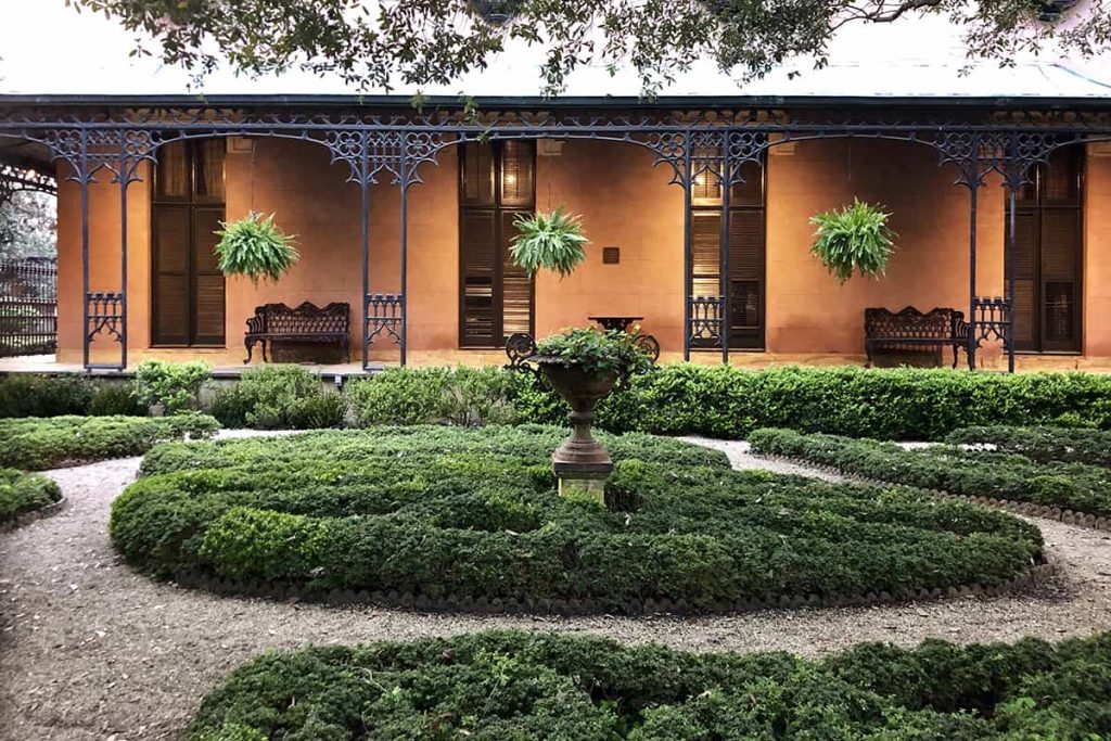 A lush green courtyard with black iron details showing on the side patio of the Green-Meldrim House
