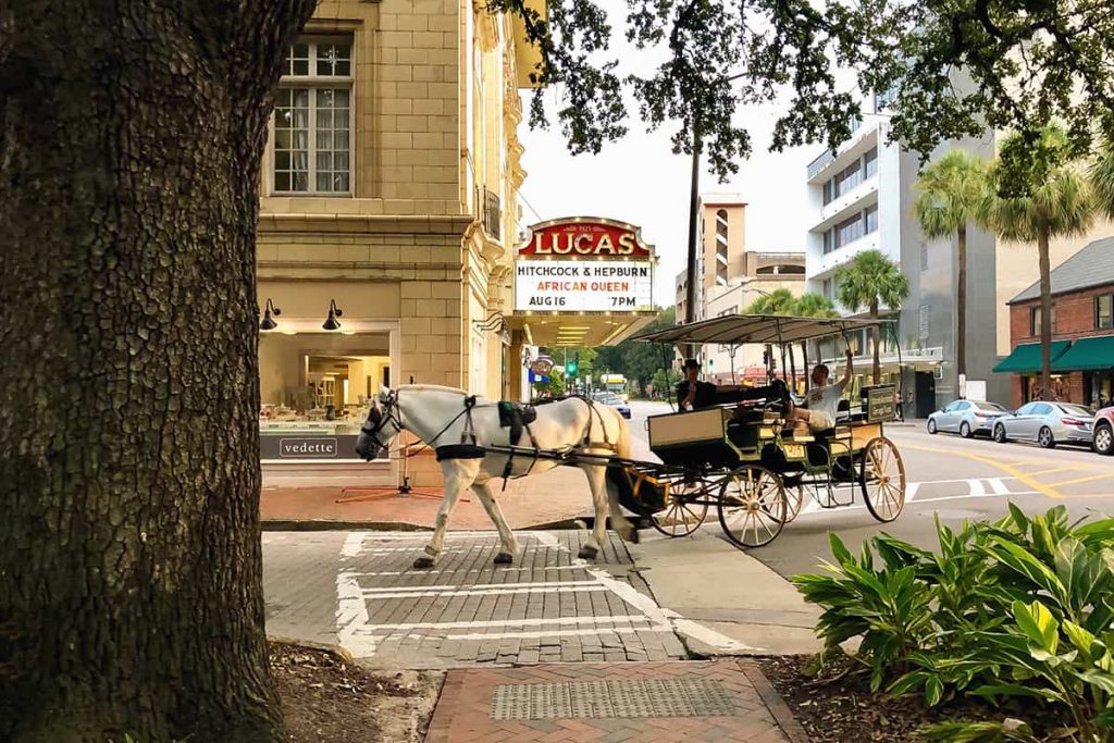 A white horse and carriage pass by the marquis lights of the Lucas Theatre sign