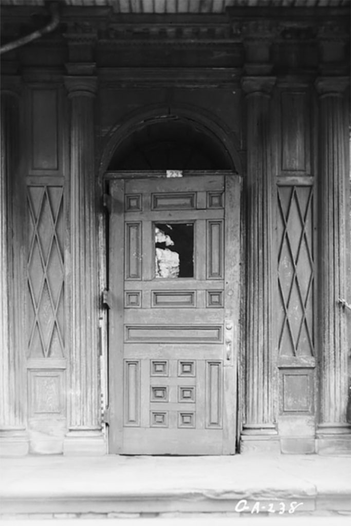 B&W image of a wooden front door and surrounding wood columns at The Olde Pink House, a haunted restaurant in Savannah