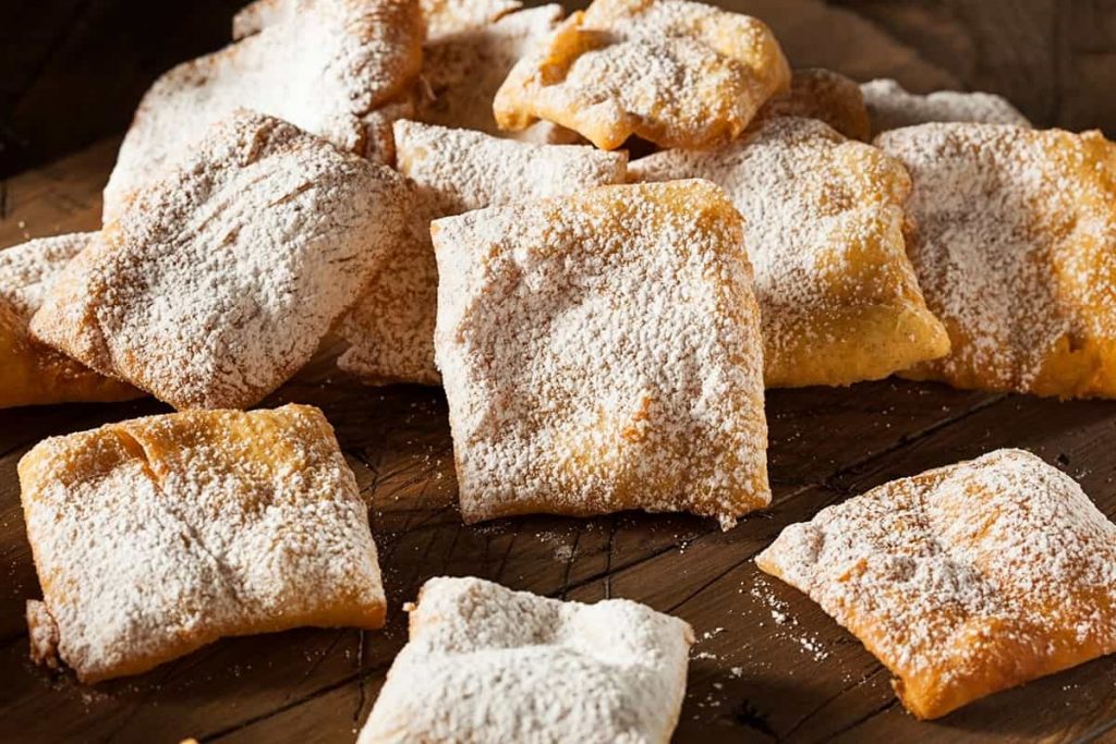 Wooden table piled high with light and flaky beignets dusted in powdered sugar