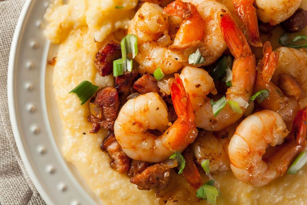 White bowl with shrimp and sausage piled atop a helping of buttery grits